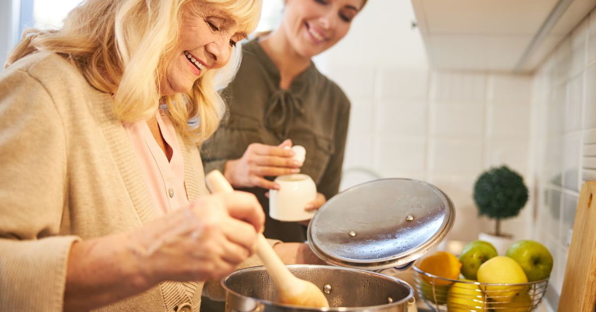 cooking-whole-foods-kitchen-stressfreelongevity Woman cooking a meal from scratch at home with fresh fruit nearby