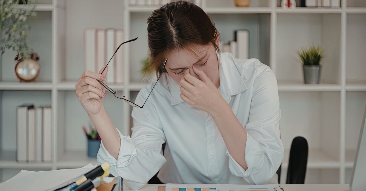 foods-fight-fatigue-featured-stressfreelongevity Professional at desk rubbing eyes with glasses removed, experiencing afternoon fatigue