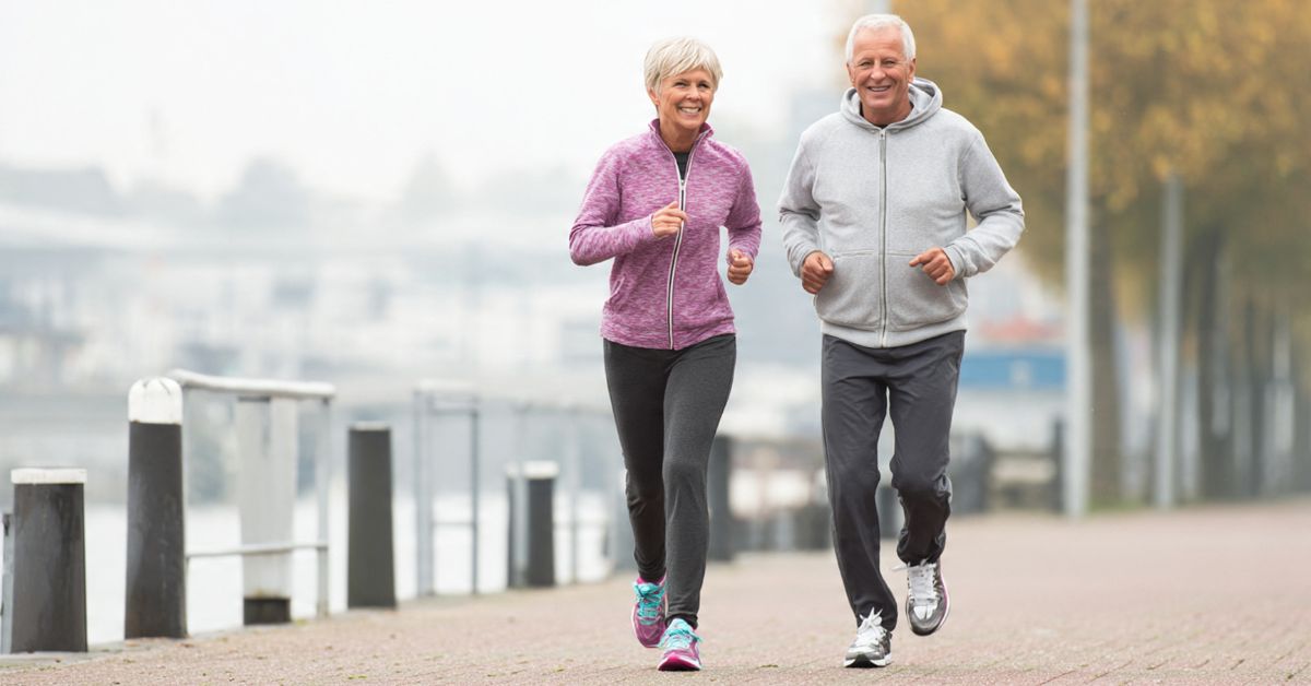 longevity-tips-never-too-late-stressfreelongevity Older couple jogging together outdoors by the waterfront — it's never too late to start