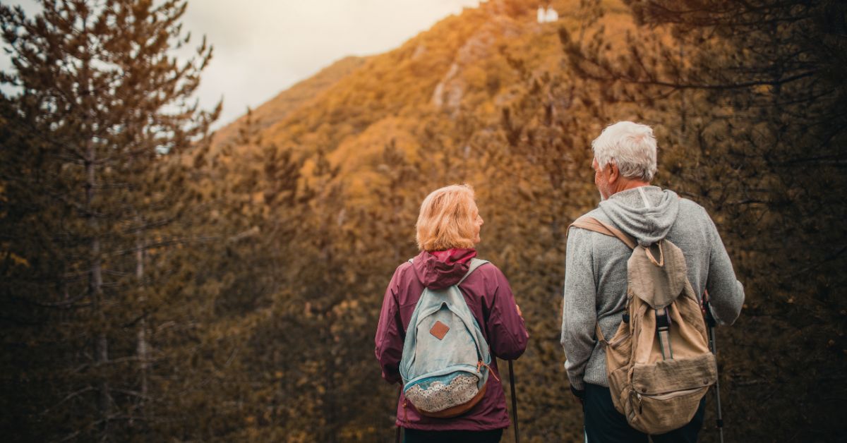 Two older adults hiking together in autumn forest, viewed from behind