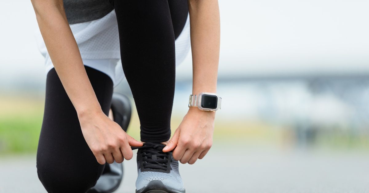 Person tying running shoe wearing smartwatch — heart rate variability tracking