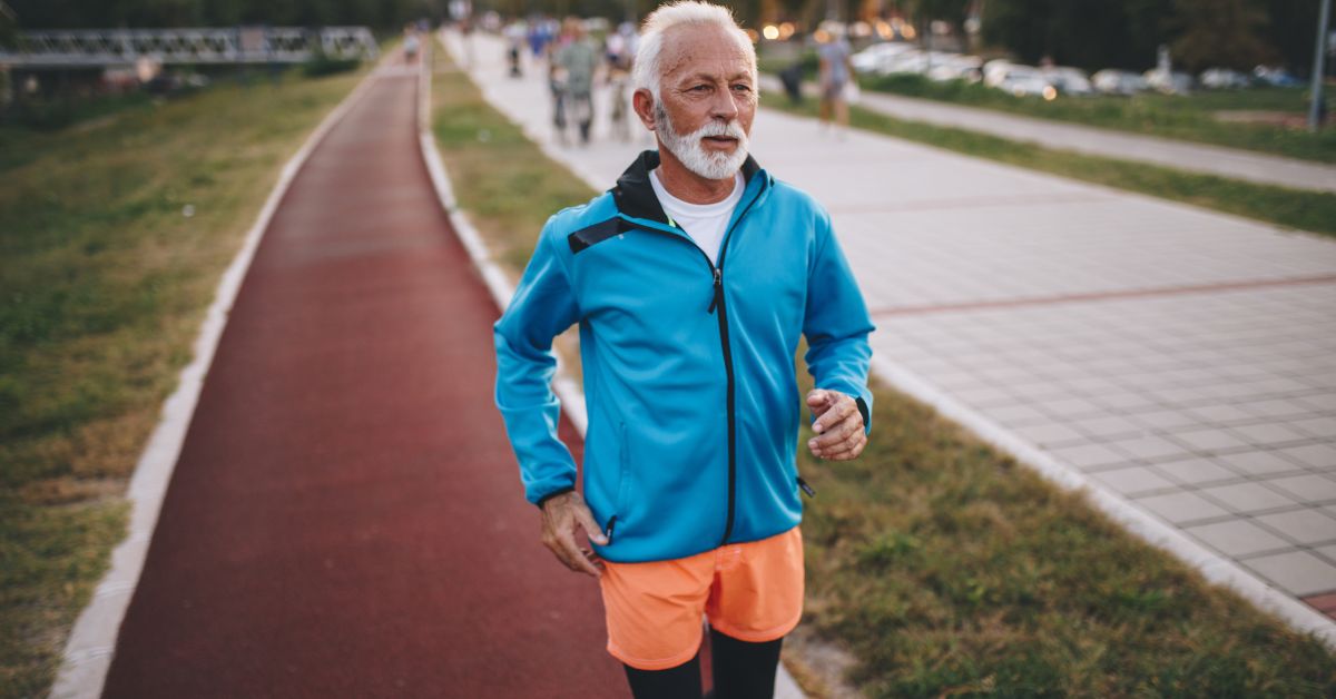 Older man jogging on an outdoor path wearing a blue sports jacket