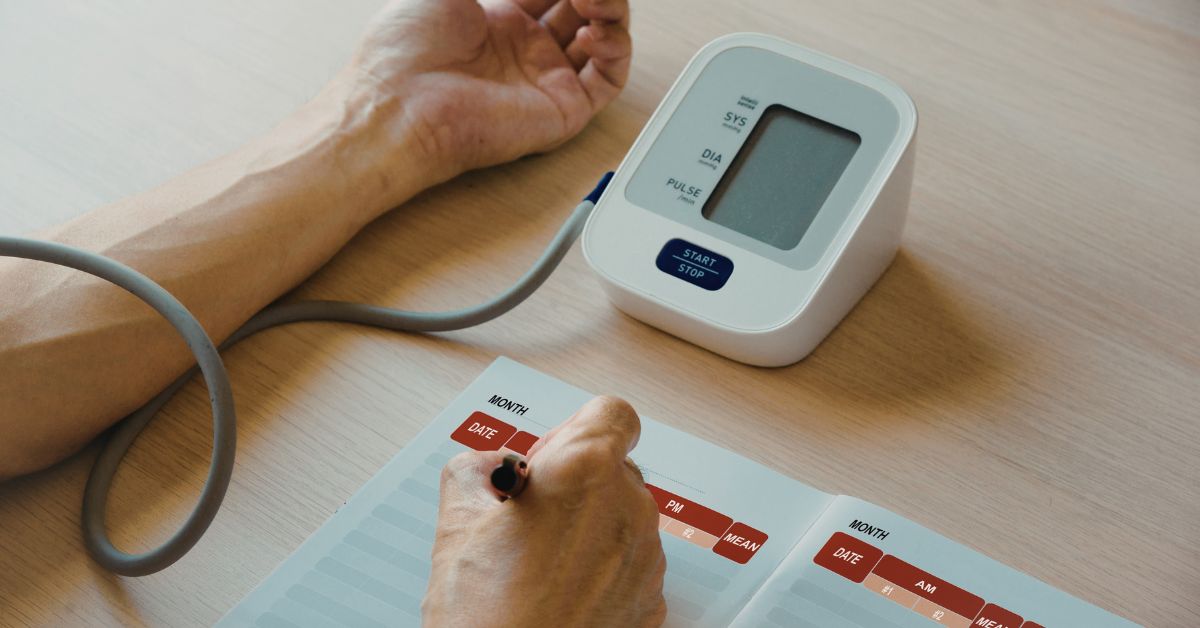 A person starting a blood pressure measurement at home using an upper-arm cuff monitor on their left arm.