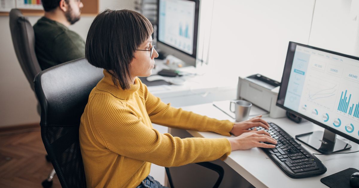 sitting-desk-working-stressfreelongevity Woman sitting at a desk working at a computer in an office