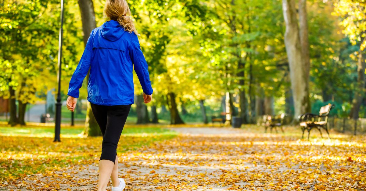 walking-park-regular-movement-stressfreelongevity Woman walking through a park in autumn — regular movement through the day