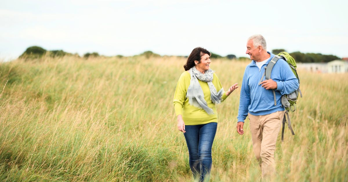 Couple in their 50s walking briskly outdoors through tall grass — illustrating the kind of sustainable, lifelong activity that supports muscle and health after 40