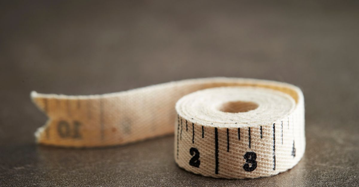 waist-to-height-ratio-tape-measure Cloth tape measure on a dark surface, used to measure your waist and calculate your waist-to-height ratio.