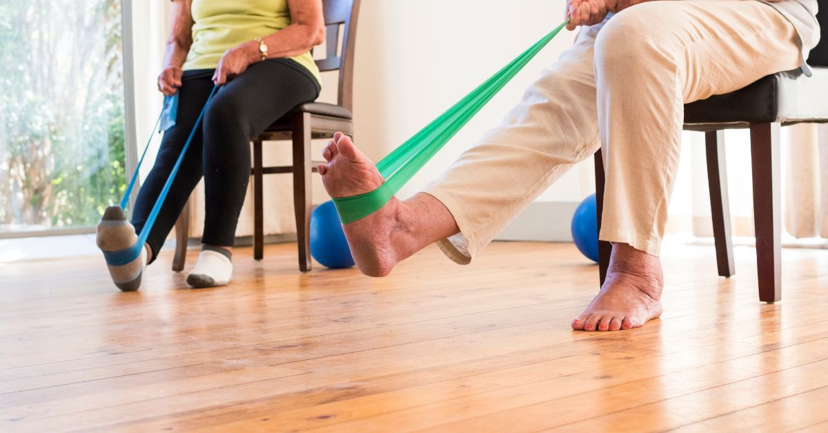 what-counts-as-strength-training-resistance-bands-stressfreelongevity Two older adults doing seated resistance band exercises at home, showing strength training doesn't need a gym