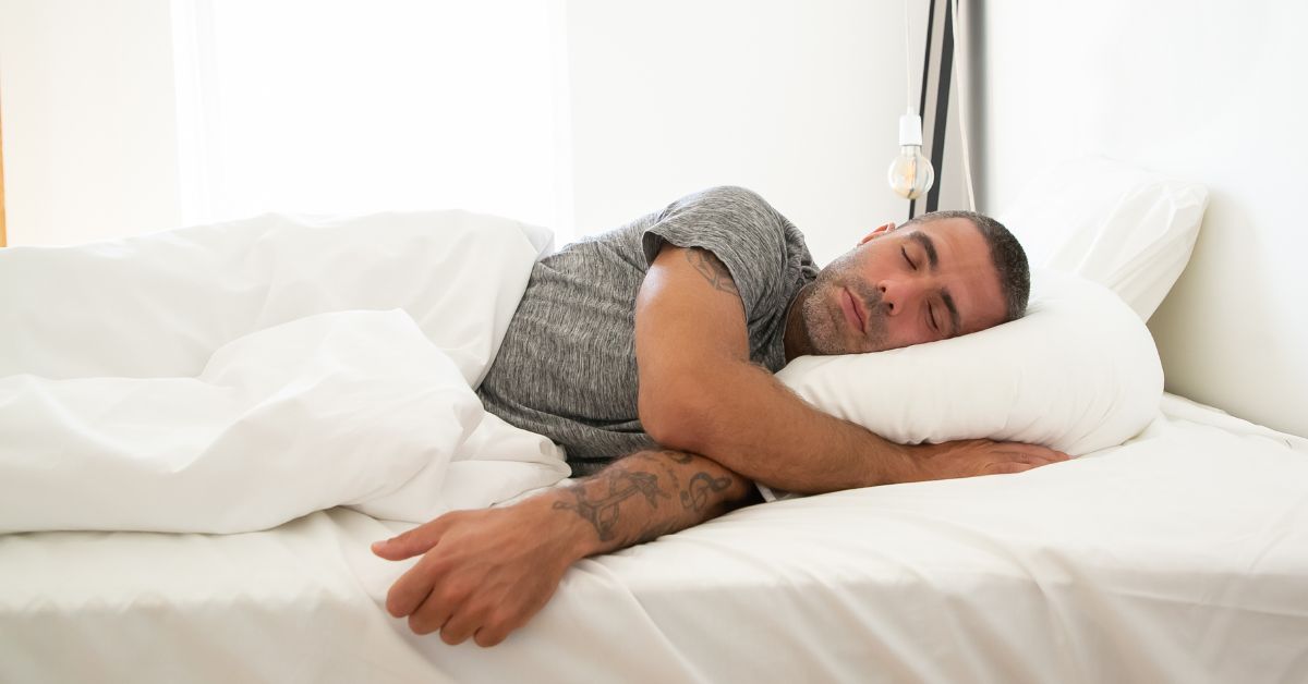 Sleep consistency and timing — a man sleeping in late as bright morning light fills the bedroom