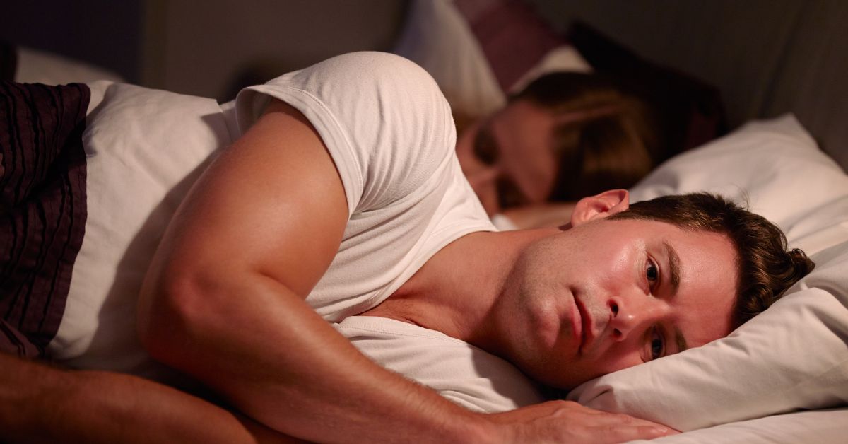 Man lying awake in bed while his partner sleeps beside him