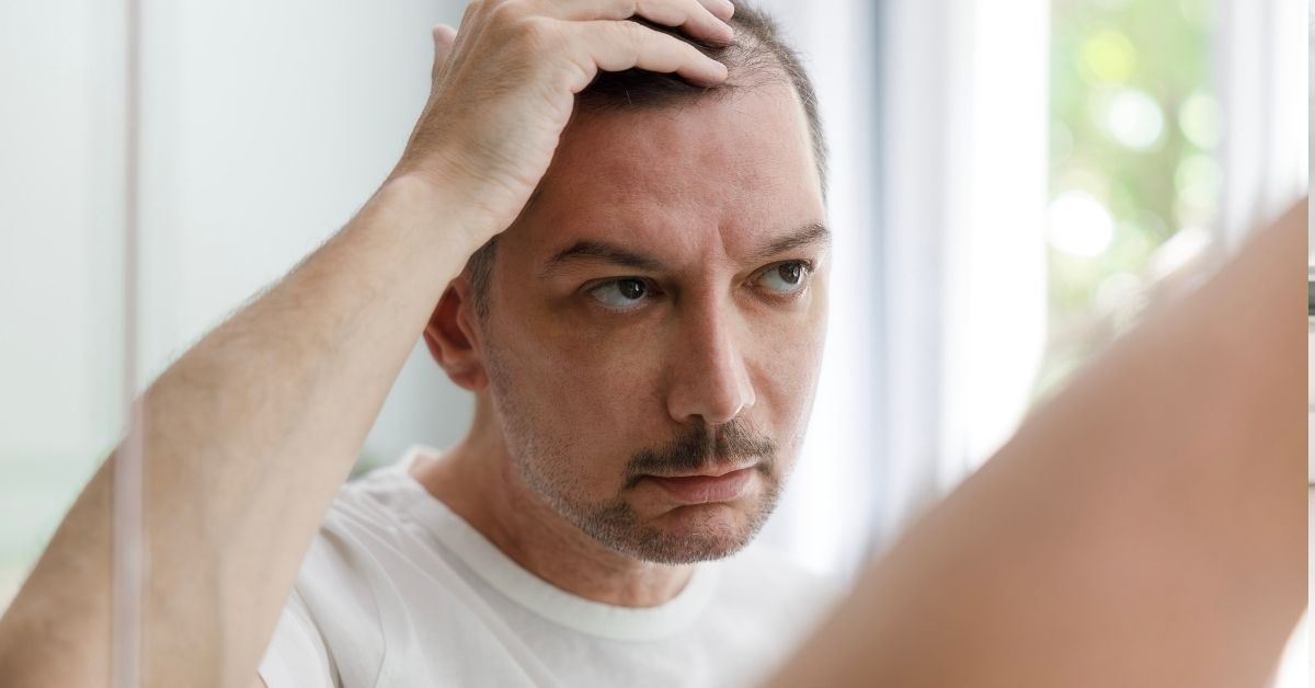 Man in his forties checking his hairline in the bathroom mirror