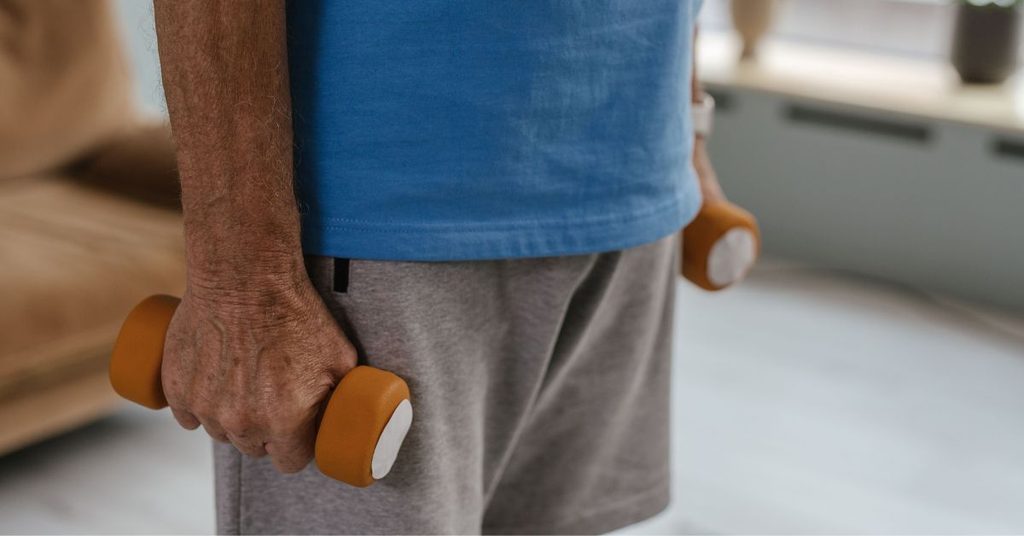 An older man holding a pair of light dumbbells in his living room